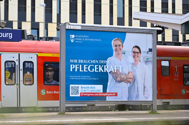 s:54:"Plakat wirbt am Bahnhof Bad Homburg für Pflegekräfte";